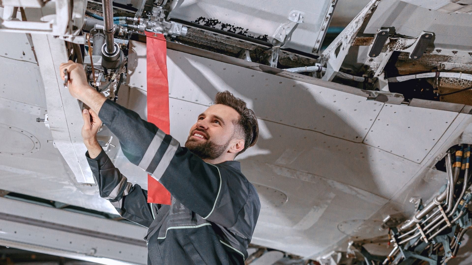 Aircraft maintenance technician in navy jumpsuit performing routine inspection on an aircraft undercarriage.